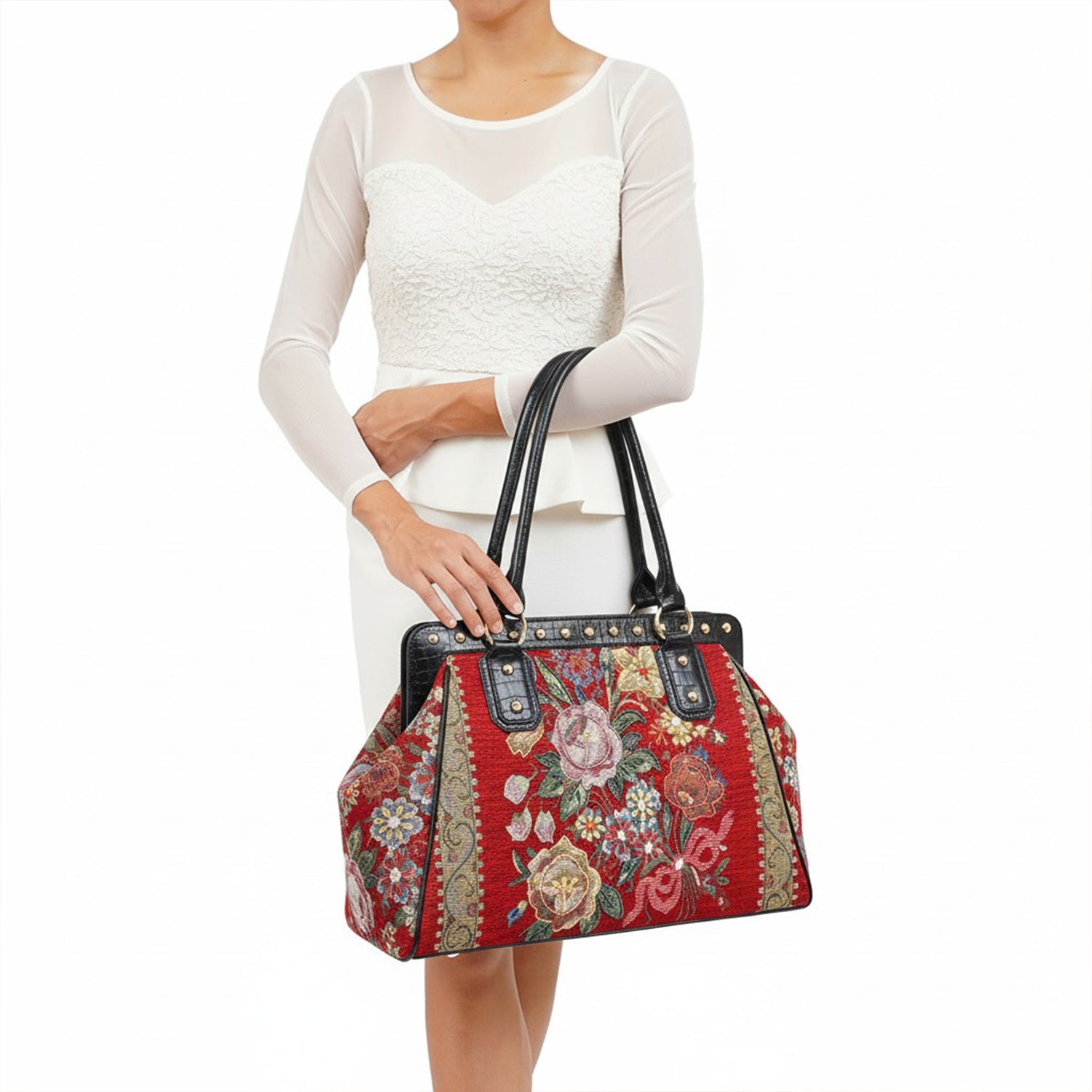 Mellow World red floral tapestry handbag with black vegan‑leather handles and gold‑tone studs, shown held by model in white lace outfit.